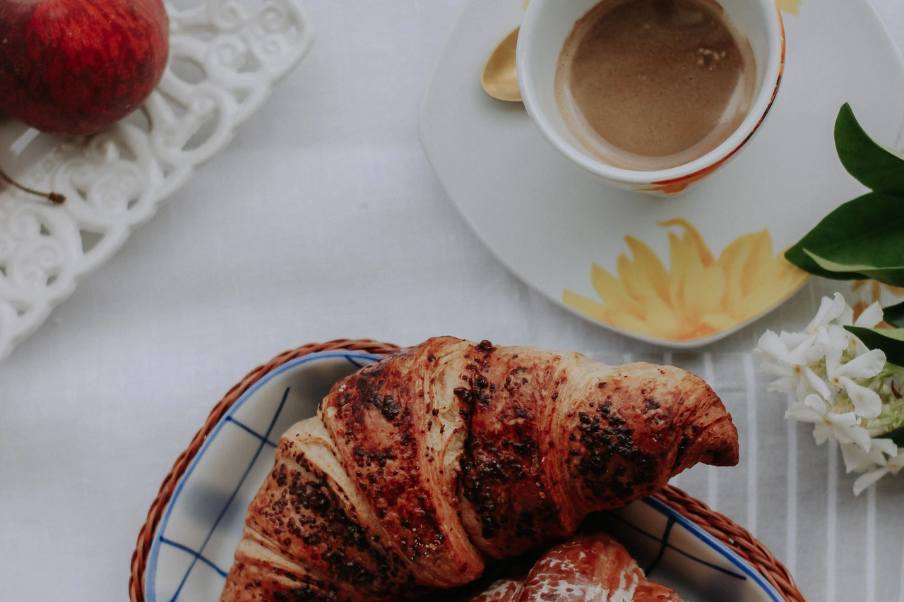 Xícara de café e croissant sobre uma mesa; fotografia ilustrativa.