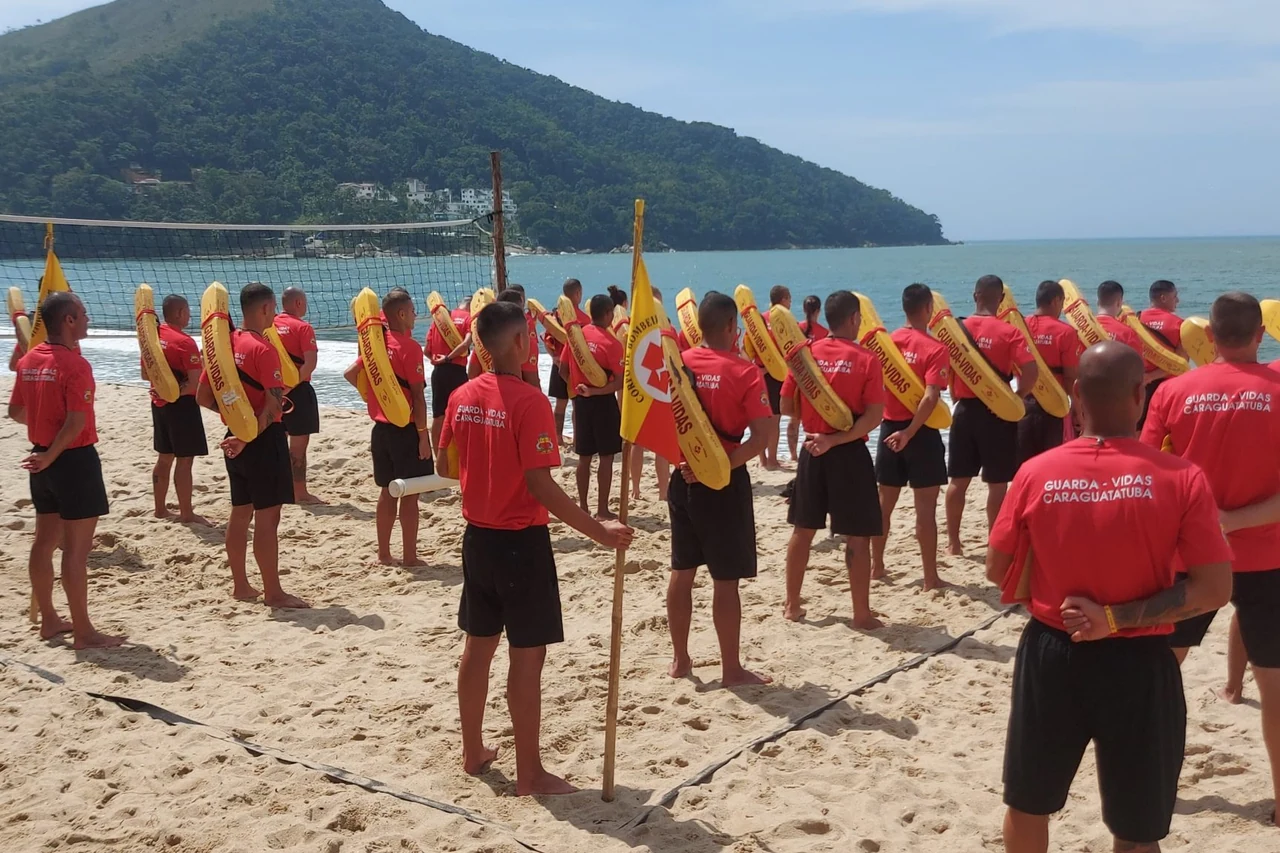 Participantes de treinamento de guarda-vidas reunidos na areia da Praia Martim de Sá, com flutuadores amarelos.