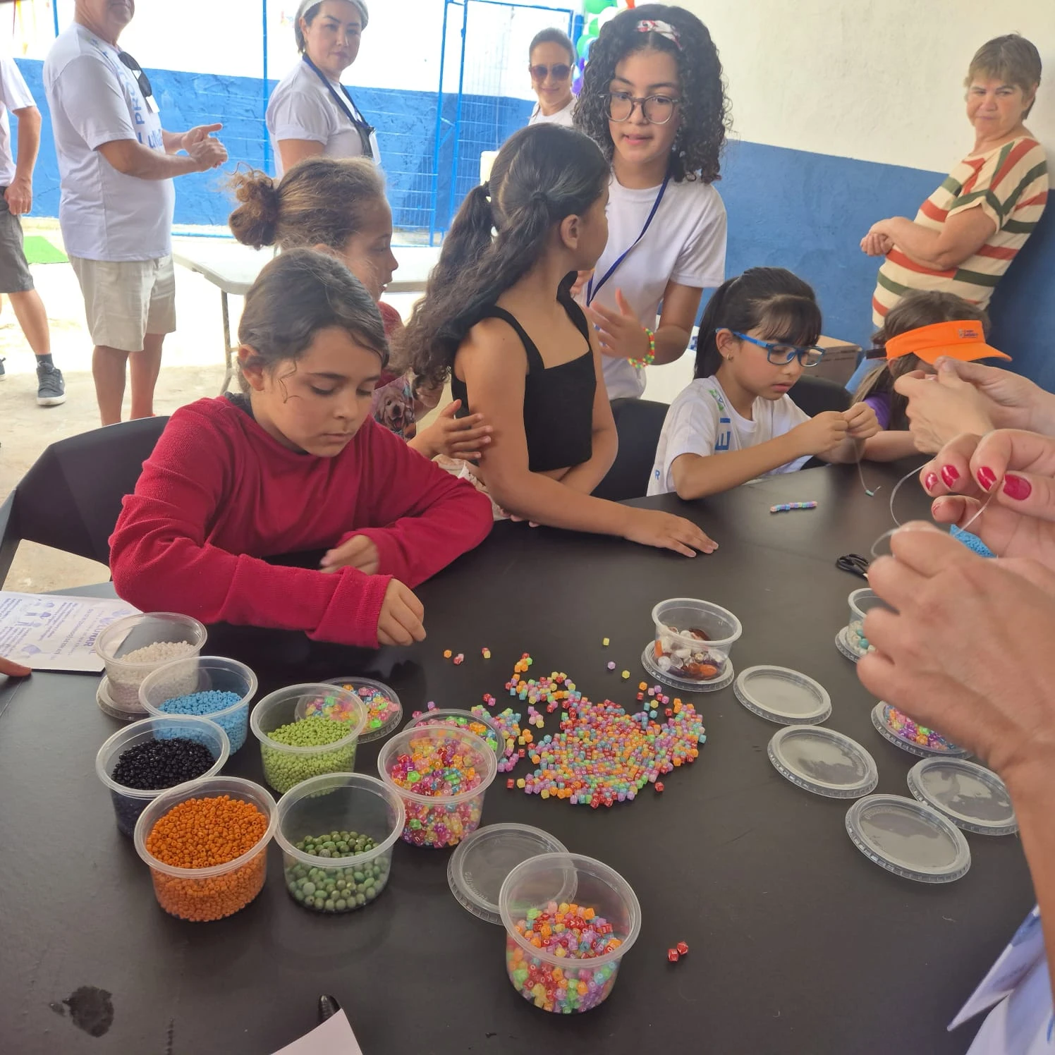 Crianças trabalham com contas coloridas em uma oficina de bijuteria.
