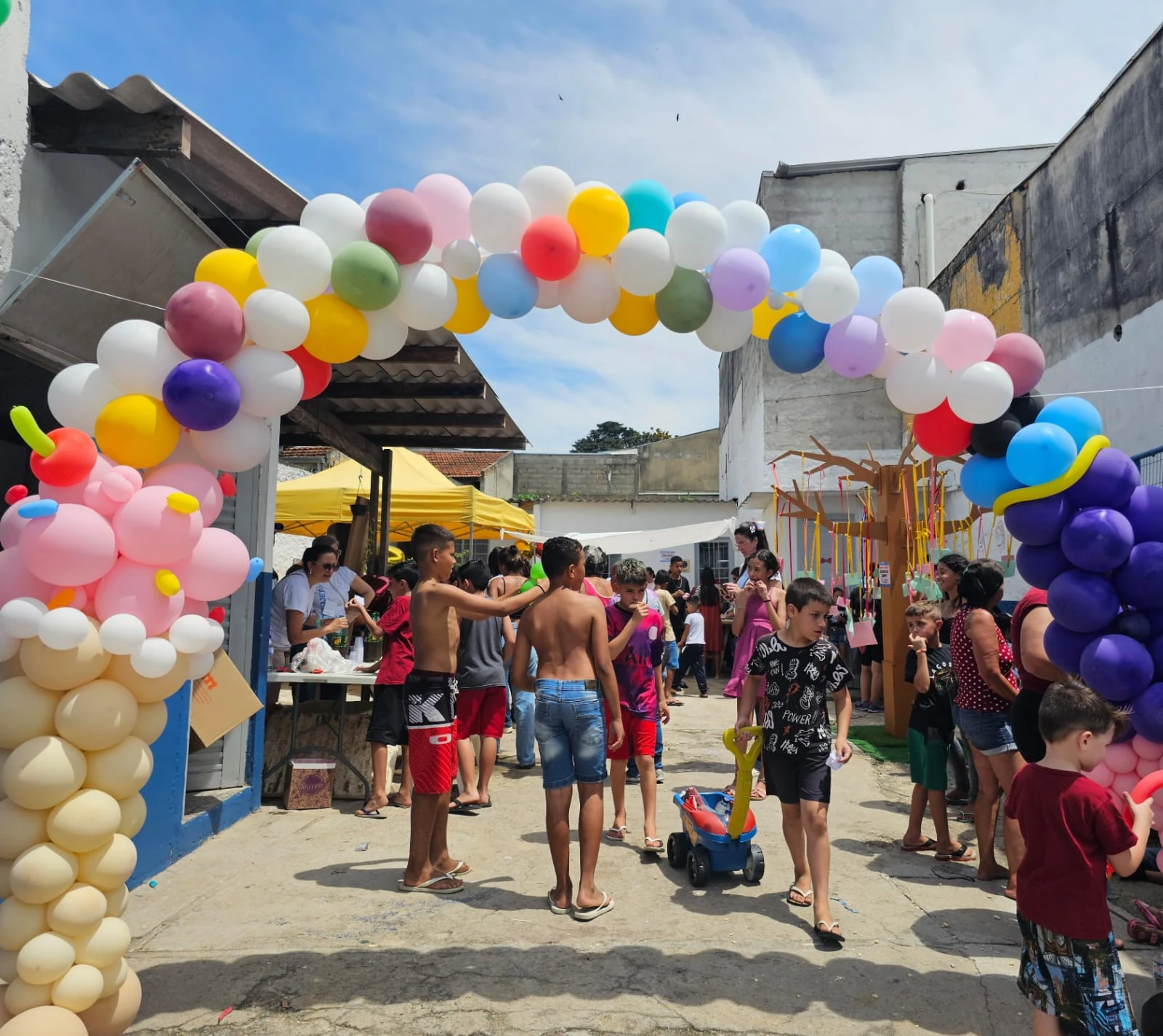Arco de balões na entrada do espaço com participantes ao fundo.