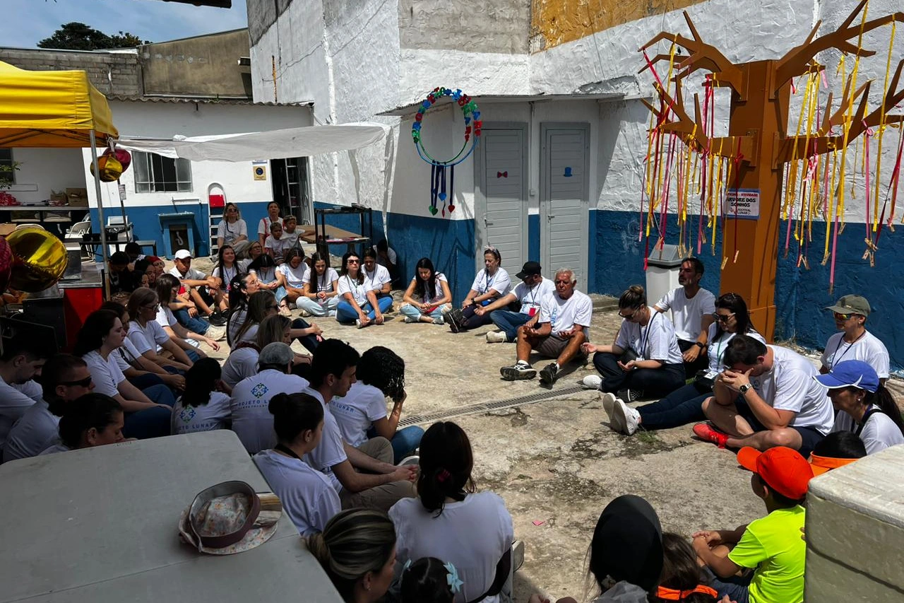 Grupo de adultos e crianças sentado em roda em espaço decorado do Projeto Lunar.