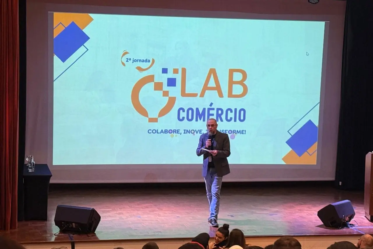 Apresentador no palco diante da projeção da 2ª Jornada Lab Comércio, em Campos do Jordão