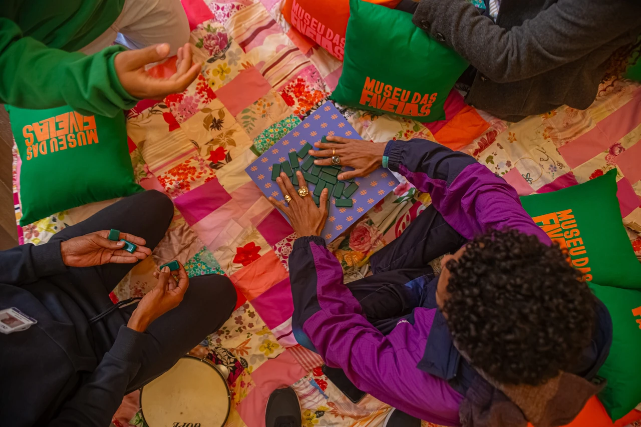 Pessoas participam de um jogo em atividade educativa do Museu das Favelas, com almofadas coloridas ao redor.