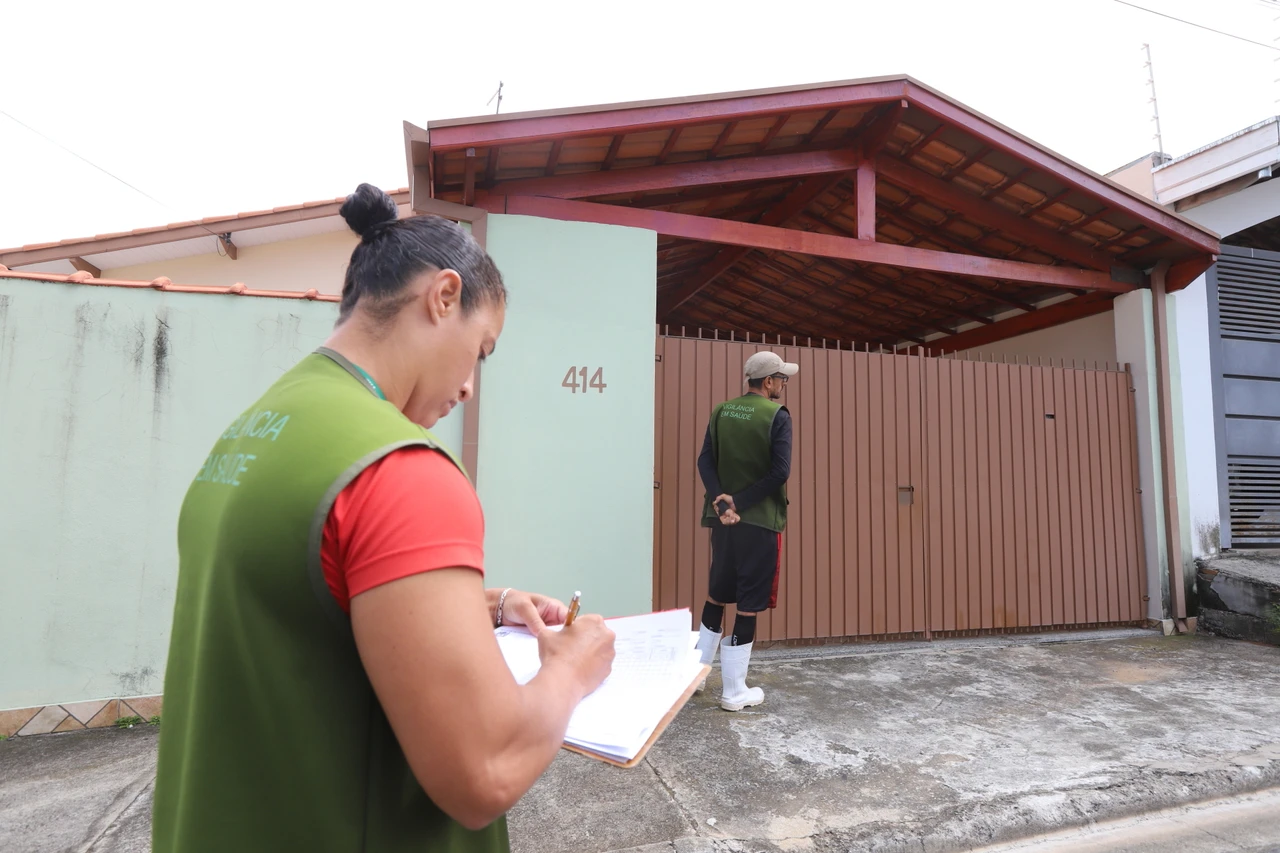 Agente com prancheta em frente a uma residência durante trabalho de campo.