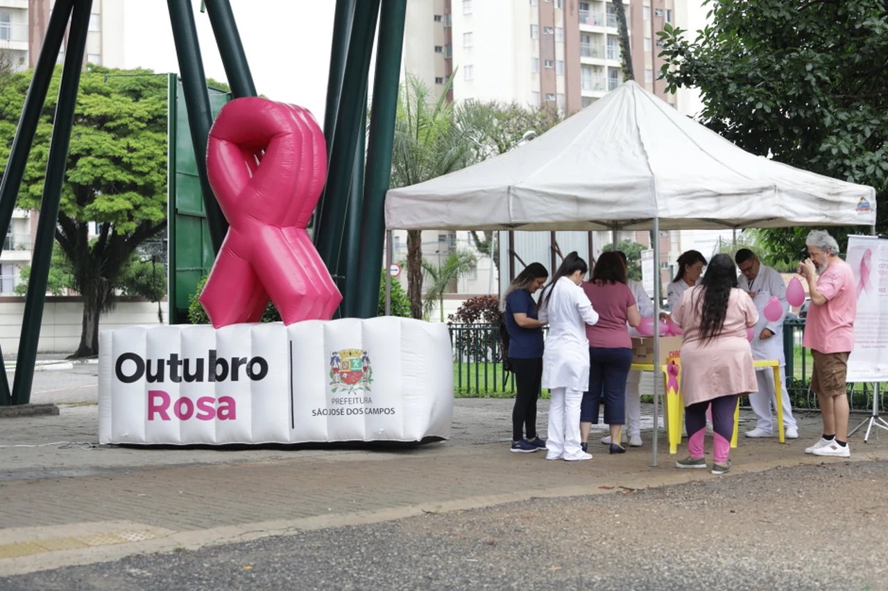 Pessoas em atendimento sob uma tenda ao lado de um laço rosa em ação de saúde de São José dos Campos.